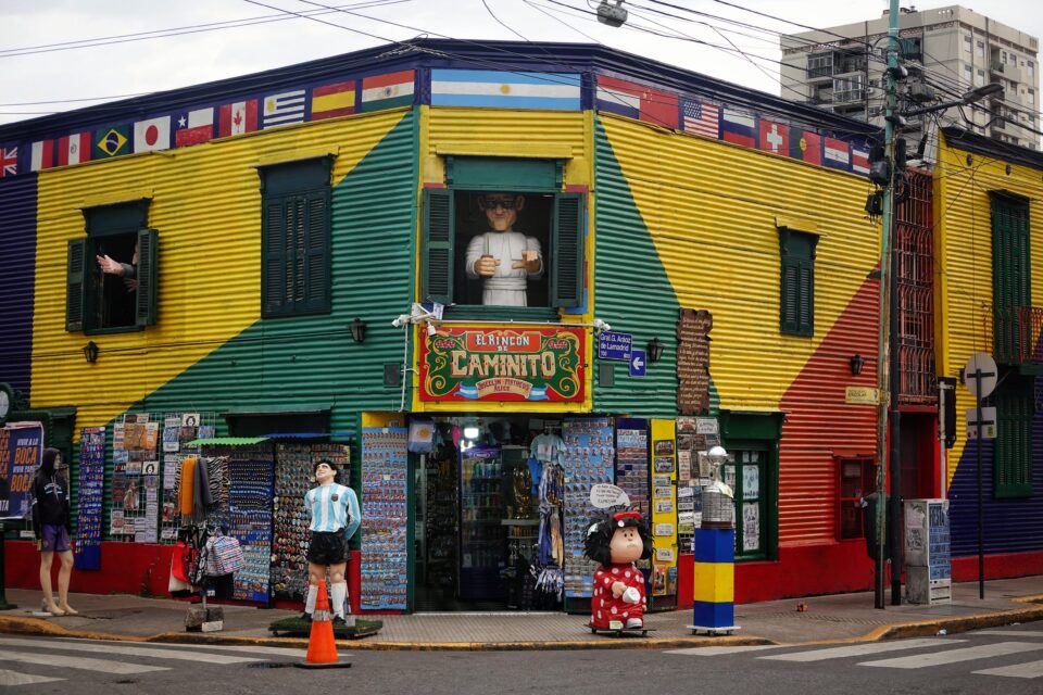 Esquina de Caminito en La Boca con fachadas de chapa amarillas, verdes y rojas, banderas y figuras en la acera