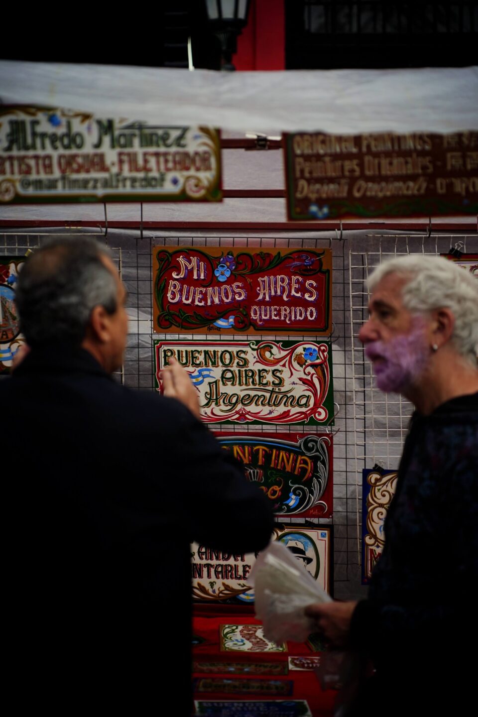 Dos vendedores del mercado de San Telmo ante un puesto cubierto de carteles y letreros de colores