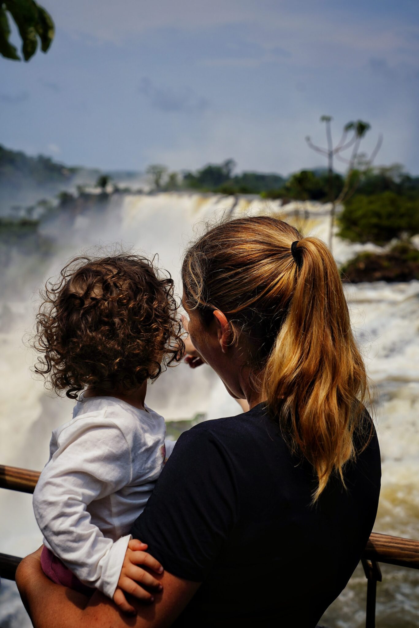 Una mujer con una niña en brazos mira las cataratas de Iguazú desde una barandilla