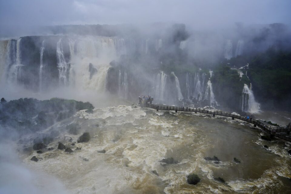Cascadas de Iguazú entre nubes de bruma sobre un río de aguas revueltas con una pasarela al fondo
